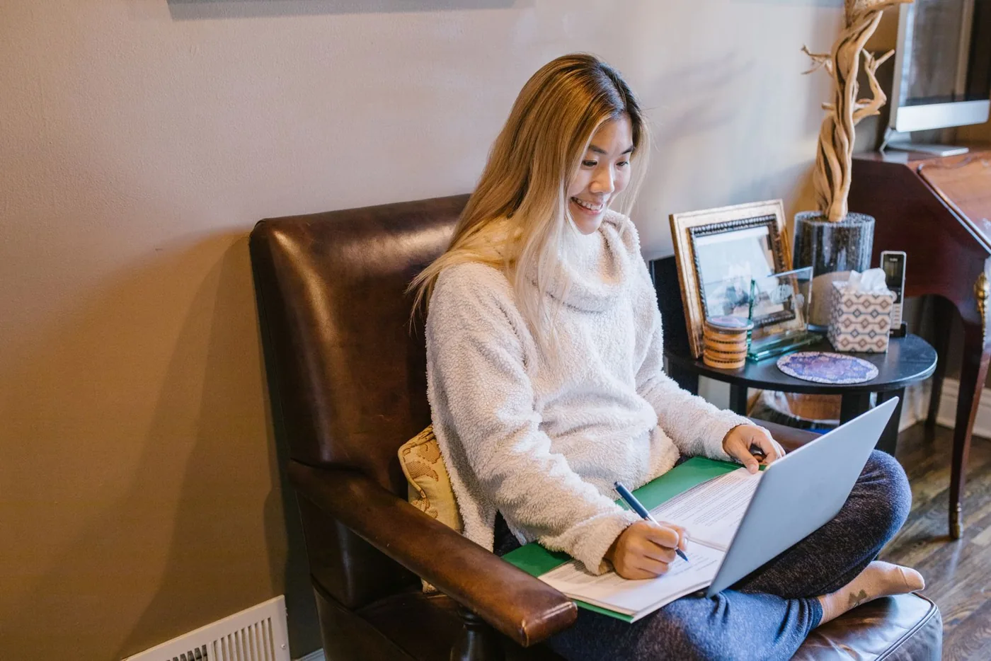 Cô gái ngồi ghế bành ghi chép bên laptop